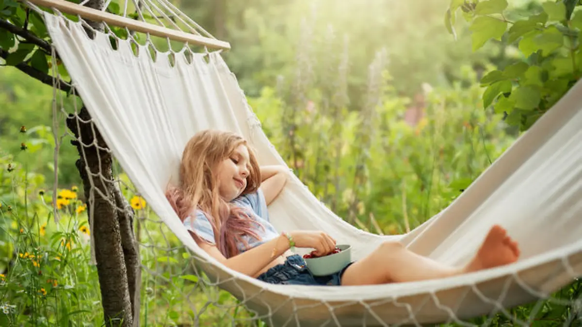 A little girl rests in a hammock and eats cherries in the summer. Summer in the village.