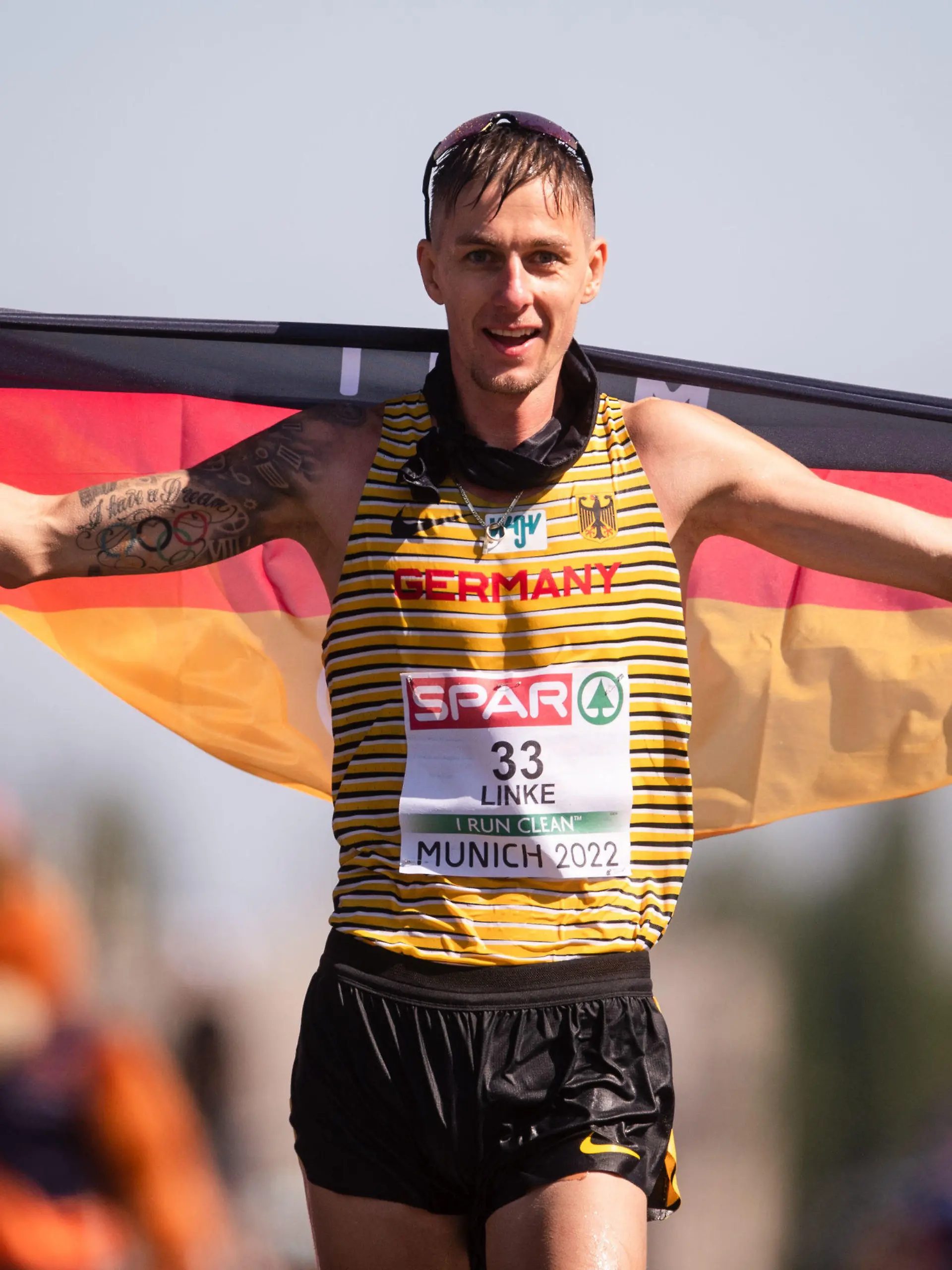 16.08.2022, Bayern, München: European Championships, Europameisterschaft, 35km Gehen Männer. Der Zweitplatzierte Christopher Linke (Deutschland) hat beim Zieleinlauf eine Fahne auf den Schultern. Foto: Marius Becker/dpa +++ dpa-Bildfunk +++