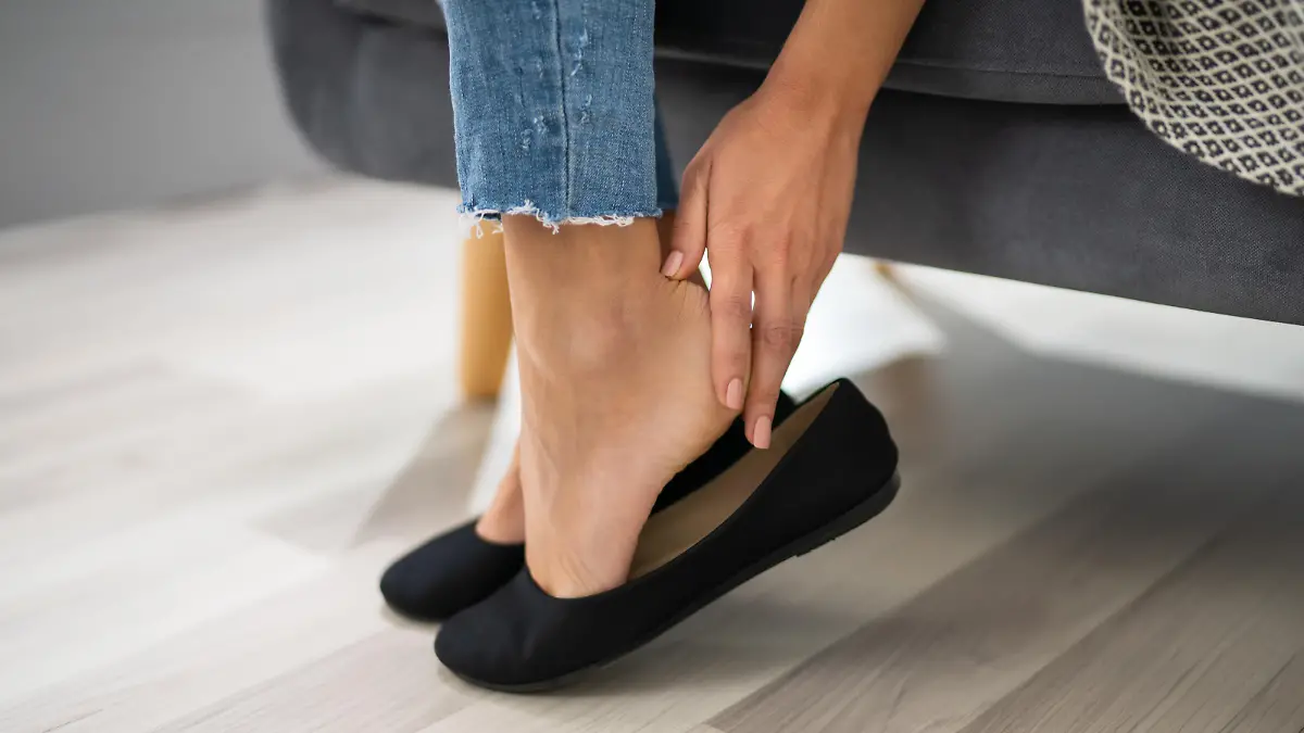 Close-up Of Woman's Hand Sitting On Sofa Removing  Uncomfortable Ballerinas