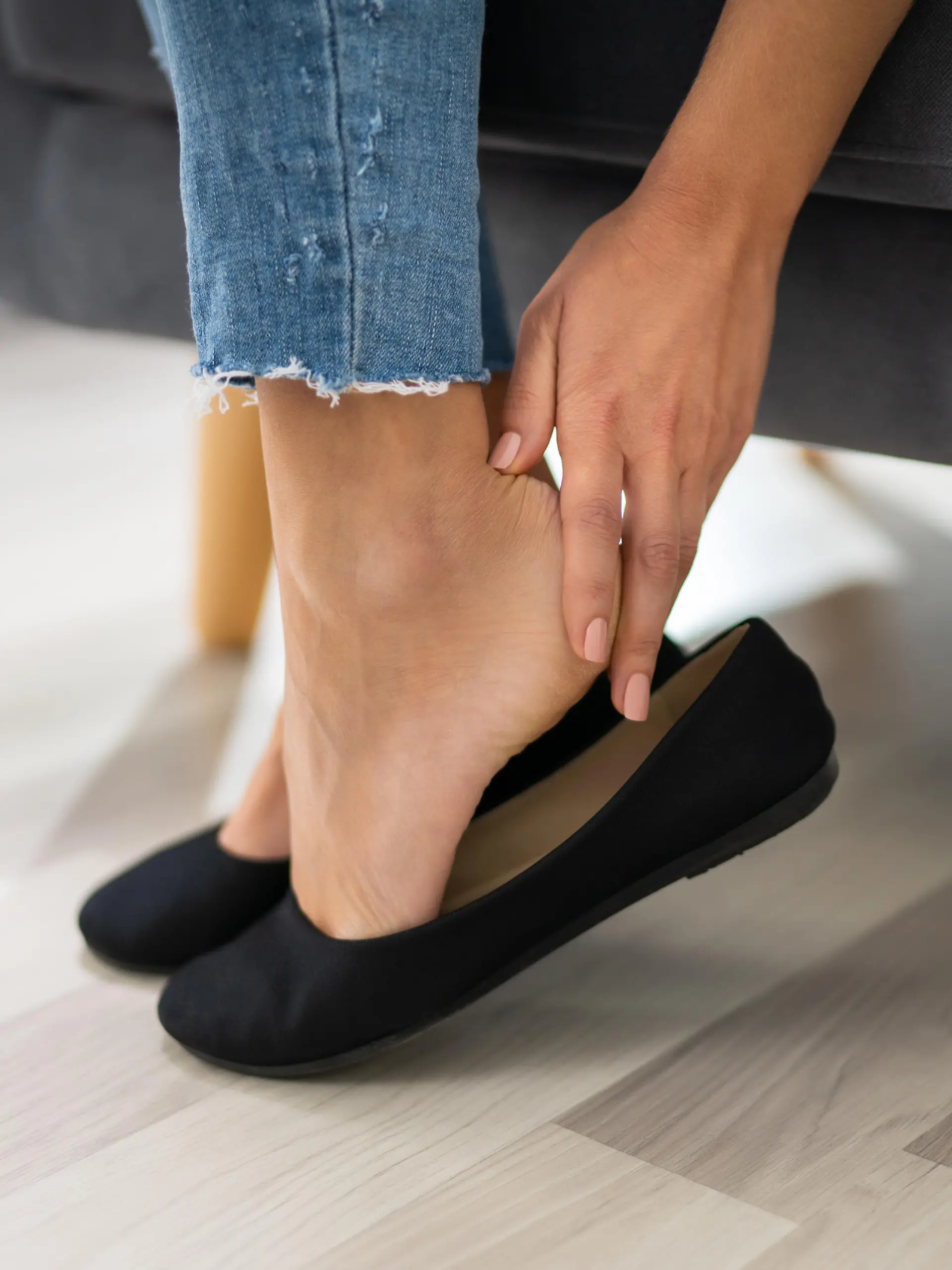 Close-up Of Woman's Hand Sitting On Sofa Removing Uncomfortable Ballerinas
