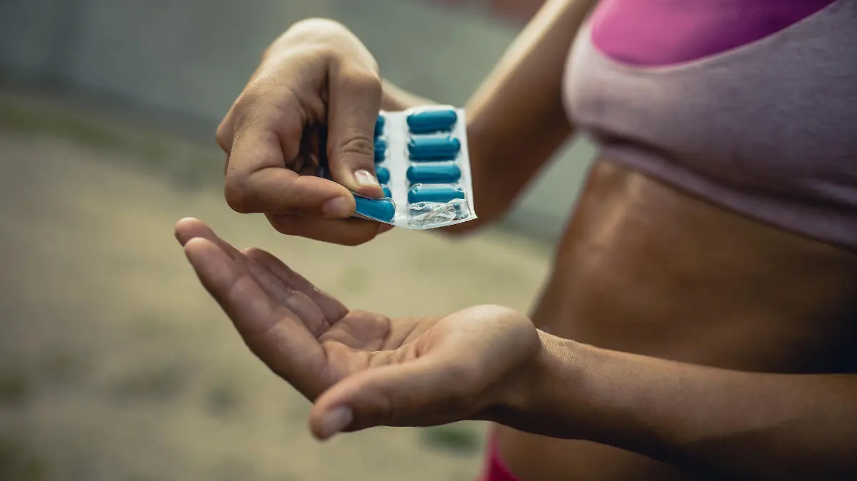 Close up of unrecognizable female athlete taking pills before sports training.