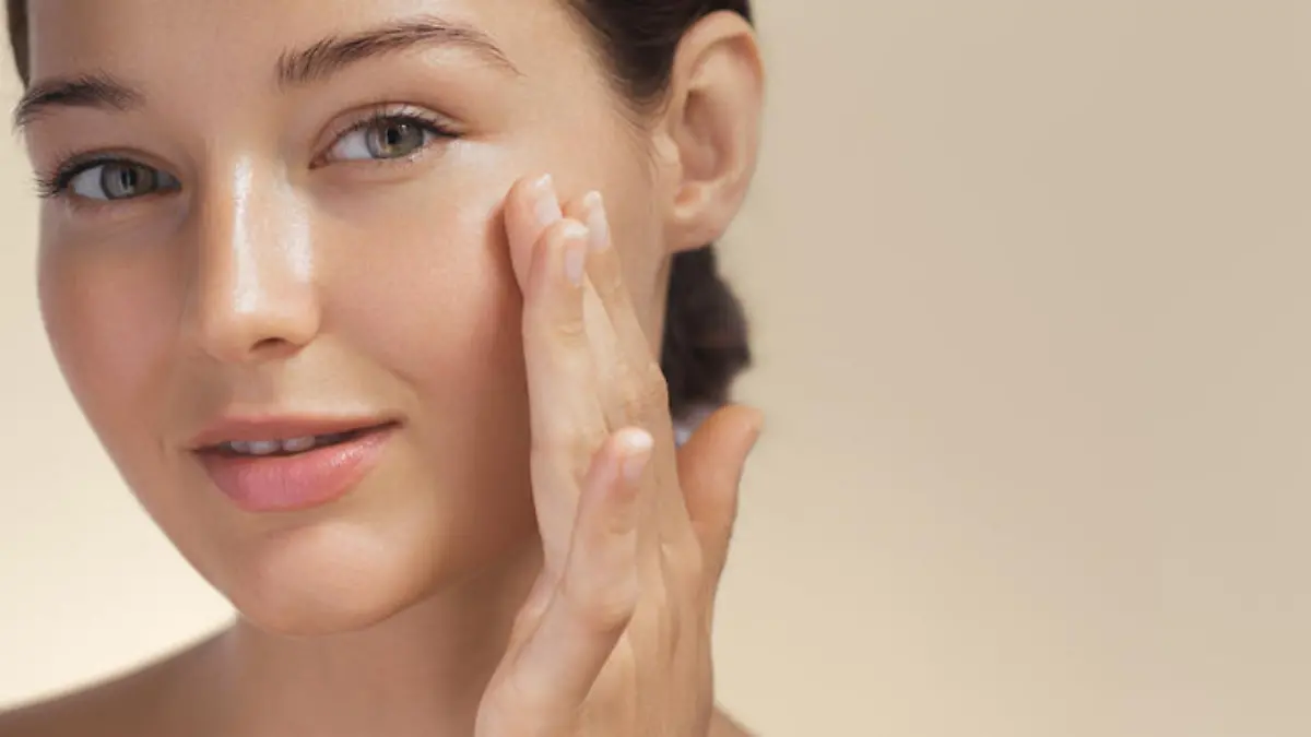 Skincare. Woman with beautiful face touching healthy facial skin portrait. Beautiful smiling Asian girl model with natural makeup enjoys glowing hydrated skin on beige background closeup. High-quality photo