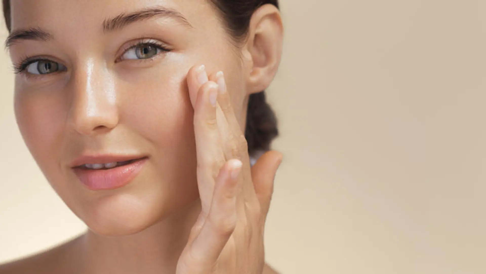 Skincare. Woman with beautiful face touching healthy facial skin portrait. Beautiful smiling Asian girl model with natural makeup enjoys glowing hydrated skin on beige background closeup. High-quality photo