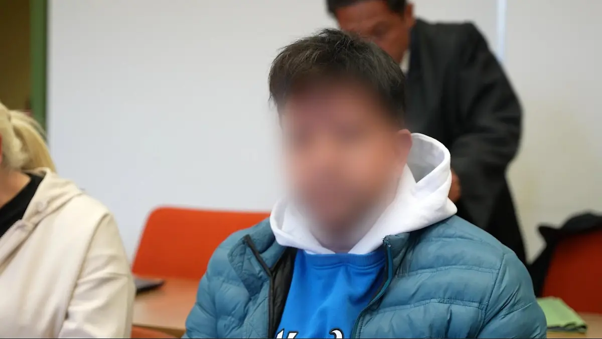 Ein angeklagter Mann sitzt auf der Anklagebank vor Gericht und schaut in die Kamera.