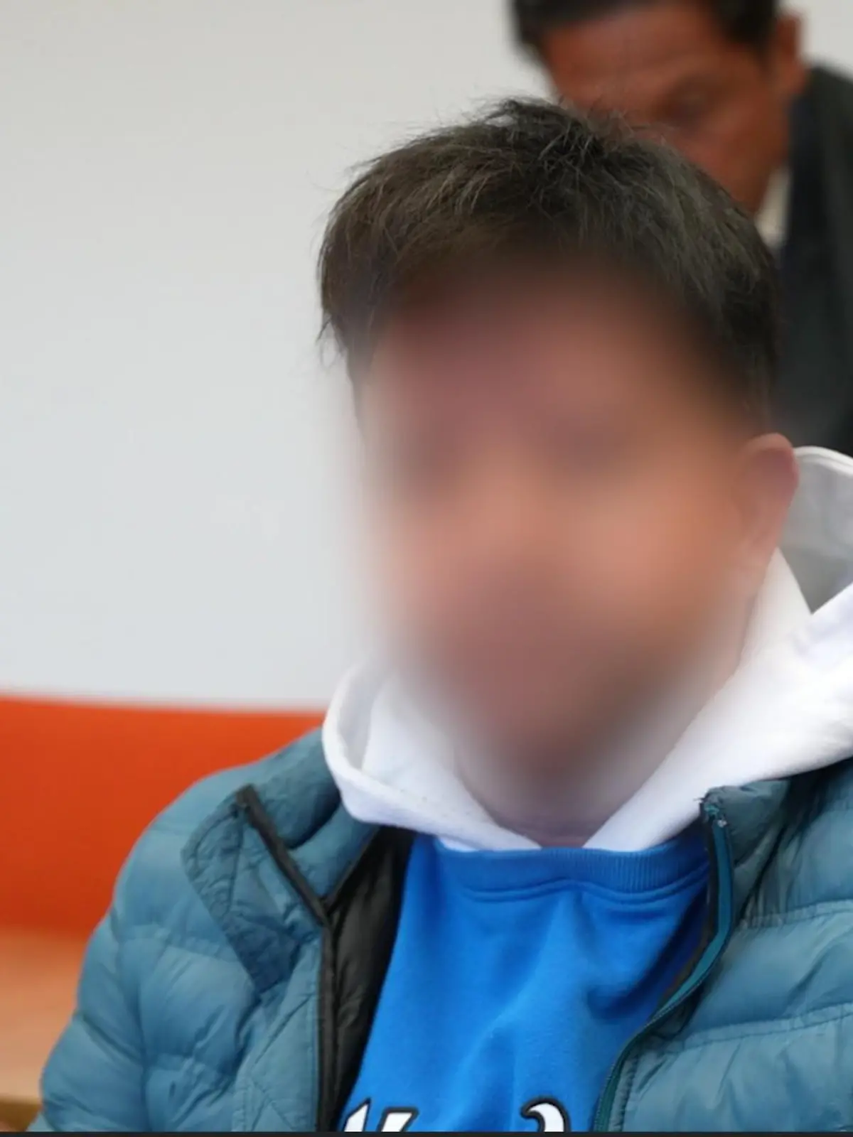 Ein angeklagter Mann sitzt auf der Anklagebank vor Gericht und schaut in die Kamera.