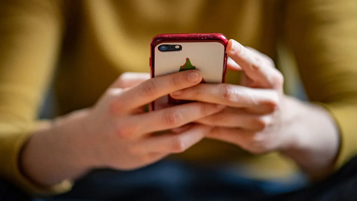 Eine junge Frau hält ein Smartphone in der Hand.