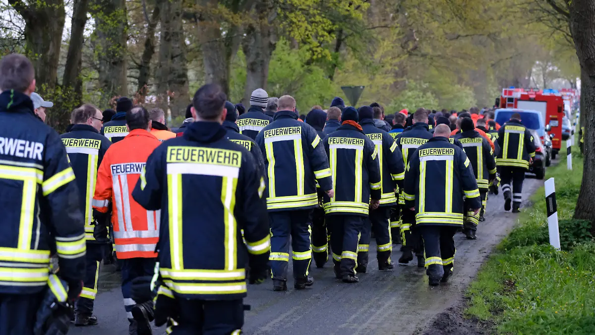 24.04.2024, Niedersachsen, Bremervörde: Feuerwehrleute laufen auf einer Straße bei Bremervörde. Von einem vermissten sechs Jahre alten Jungen aus dem niedersächsischen Bremervörde fehlt noch immer jede Spur. Foto: Markus Hibbeler/dpa +++ dpa-Bildfunk +++