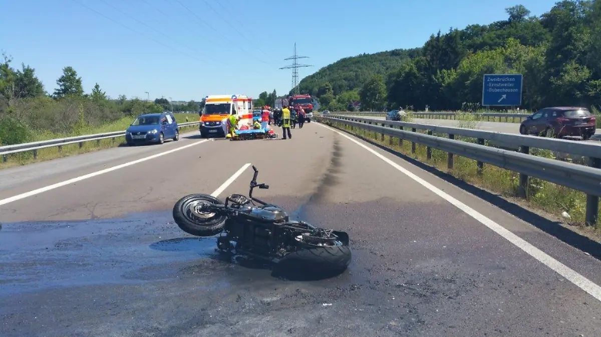 01.07.2018, Rheinland-Pfalz, Zweibrücken: Ein beschädigtes Motorrad liegt auf der Fahrbahn der gesperrten Autobahn 8. Dahinter stehen Sanitäter an einem Krankenwagen. Ein 13 Jahre alter Beifahrer eines Motorrads ist auf der Autobahn 8 ums Leben gekommen, weil ein Auto wohl aufgefahren ist. Achtung: Bestmögliche Qualität. (zu dpa «Auffahrunfall mit Fahrerflucht auf A8 endet für 13-Jährigen tödlich» vom 01.07.2018) Foto: -/Polizei Zweibrücken/dpa - ACHTUNG: Nur zur redaktionellen Verwendung und nur mit vollständiger Nennung des vorstehenden Credits +++ dpa-Bildfunk +++