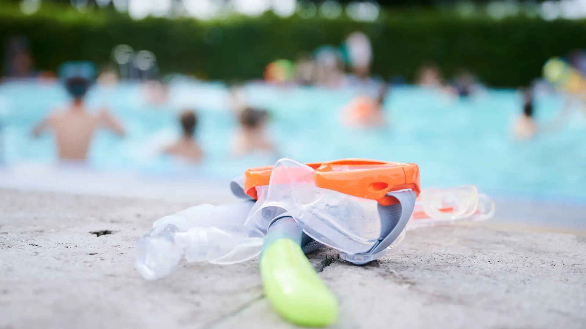 Eine Taucherbrille und Schnorchel liegen in einem Schwimmbad am Beckenrand.