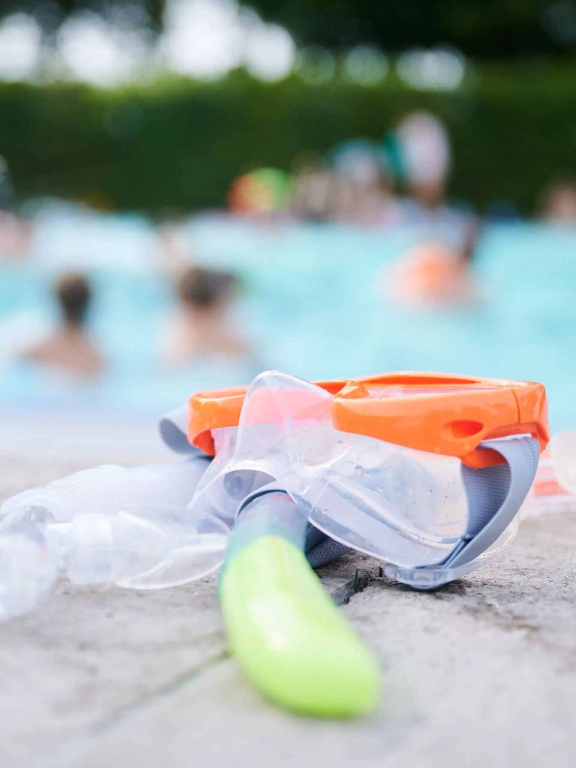 Eine Taucherbrille und Schnorchel liegen in einem Schwimmbad am Beckenrand.