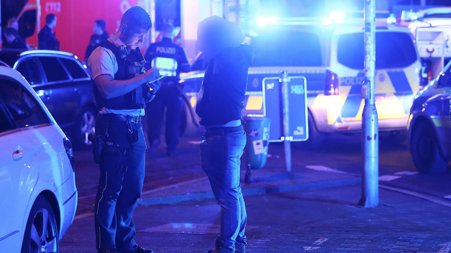 28.04.2024, Nordrhein-Westfalen, Düsseldorf: Ein Polizist befragt einen Zeugen vor einem Tatort in Düsseldorf Ortsteil Friedrichstadt.  Bei Schüssen in Düsseldorf am Sonntagmorgen ist ein Mensch getötet worden. Foto: David Young/dpa +++ dpa-Bildfunk +++