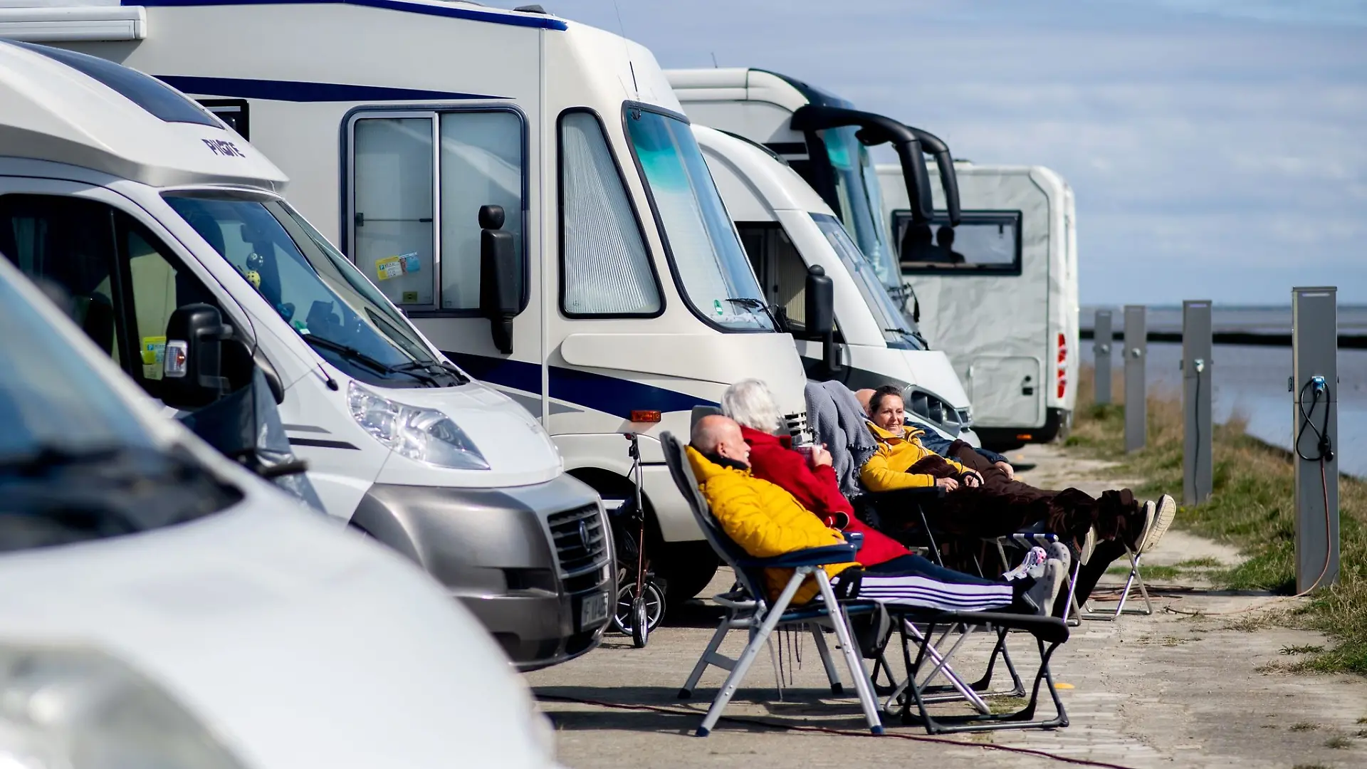 Touristen aus Nordrhein-Westfalen sitzen bei sonnigem Wetter vor ihren Wohnmobilen und blicken auf das Wattenmeer.