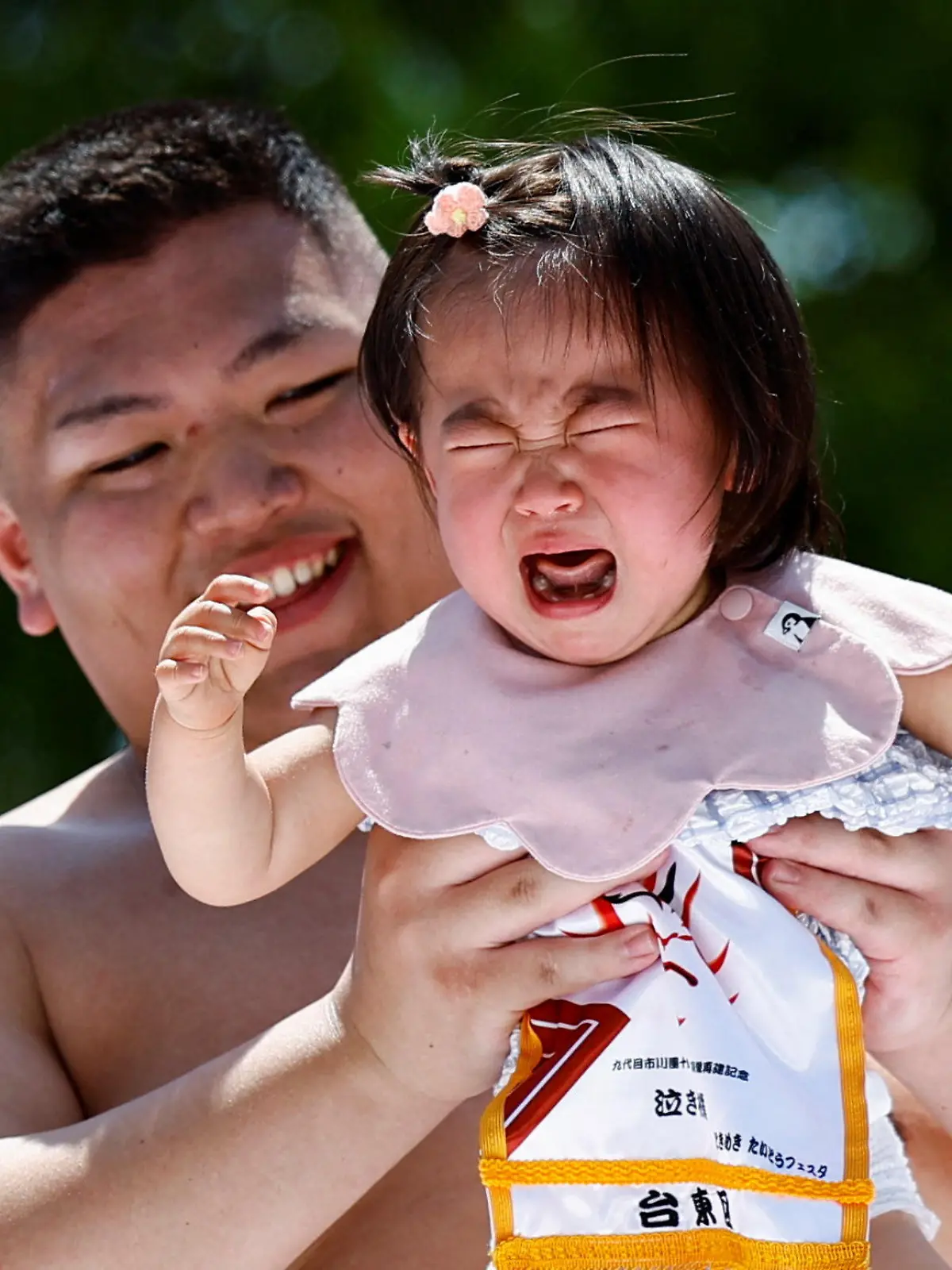 A baby cries while held up by an amateur sumo wrestler during 'Nakizumo' or a baby-crying sumo contest, where two wrestlers hold a baby each and a referee makes faces and loud noises to make them cry and determine the winner based on the loudest baby, at Sensoji temple in Tokyo, Japan, April 28, 2024. The ritual is believed to aid the healthy growth of the children and ward off evil spirits. REUTERS/Issei Kato