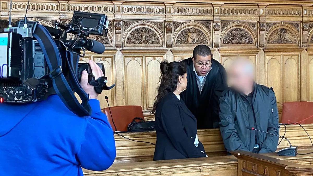 29.04.2024, Bremen: Der Angeklagte (r) steht vor Beginn des Prozesses mit seinem Anwalt Temba Hoch (hinten) und einer Dolmetscherin im Gerichtssaal im Landgericht Bremen. Er ist zu 13 Jahren Haft und Maßregelvollzug wegen Mordes an seinem siebenjährigen Sohn verurteilt worden. Foto: Janet Binder/dpa - ACHTUNG: Angeklagter wurde auf Anweisung des Gerichts aus rechtlichen Gründen gepixelt +++ dpa-Bildfunk +++