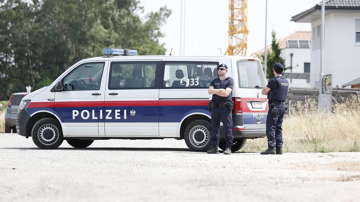 24.07.2023, Österreich, Absdorf: Polizisten stehen in der Nähe des mutmaßlichen Tatorts neben einem Polizeifahrzeug. In Österreich soll eine Mutter ihre beiden Kinder getötet haben. Anschließend soll die 36-Jährige in Suizidabsicht mit dem Auto gegen einen Baum gefahren sein. Foto: Tobias Steinmaurer/APA/dpa +++ dpa-Bildfunk +++