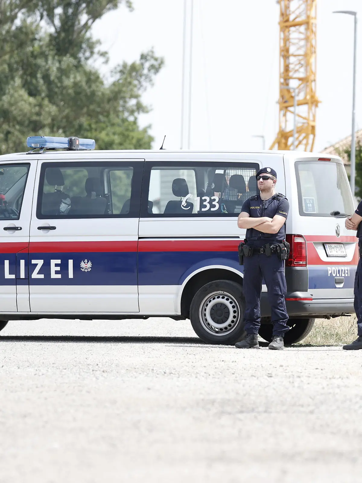 24.07.2023, Österreich, Absdorf: Polizisten stehen in der Nähe des mutmaßlichen Tatorts neben einem Polizeifahrzeug. In Österreich soll eine Mutter ihre beiden Kinder getötet haben. Anschließend soll die 36-Jährige in Suizidabsicht mit dem Auto gegen einen Baum gefahren sein. Foto: Tobias Steinmaurer/APA/dpa +++ dpa-Bildfunk +++