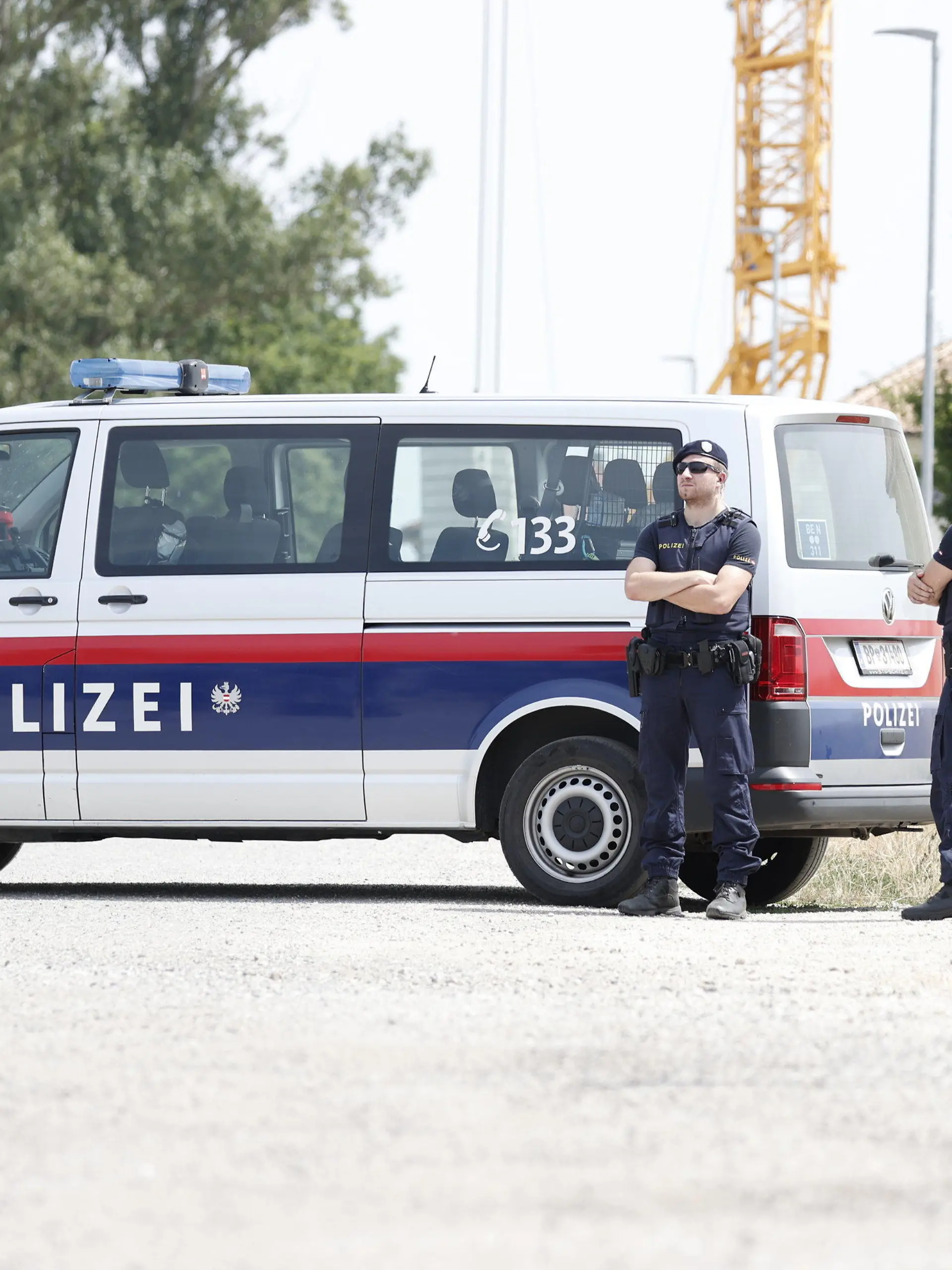 24.07.2023, Österreich, Absdorf: Polizisten stehen in der Nähe des mutmaßlichen Tatorts neben einem Polizeifahrzeug. In Österreich soll eine Mutter ihre beiden Kinder getötet haben. Anschließend soll die 36-Jährige in Suizidabsicht mit dem Auto gegen einen Baum gefahren sein. Foto: Tobias Steinmaurer/APA/dpa +++ dpa-Bildfunk +++