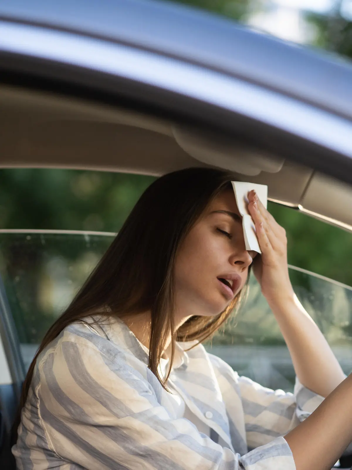 Eine Frau im Auto die sich an den Kopf fast, weil es zu heiß ist.