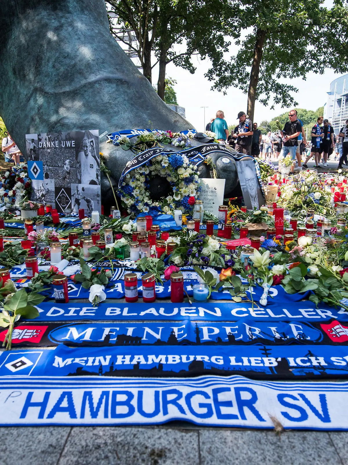 24.07.2022, Hamburg: Zahlreiche Blumen, Kerzen und Schals liegen und stehen vor dem Fußball-Zweitligaspiel Hamburger SV - Hansa Rostock vor einer Bronze vor dem Volksparkstadion, die den Fuß des ehemaligen Fußballspielers Uwe Seeler abbildet. Seeler ist im Alter von 85 Jahren gestorben. (zu dpa «Große Feier für großartigen Menschen: Abschied von Uwe Seeler») Foto: Daniel Bockwoldt/dpa - WICHTIGER HINWEIS: Gemäß den Vorgaben der DFL Deutsche Fußball Liga bzw. des DFB Deutscher Fußball-Bund ist es untersagt, in dem Stadion und/oder vom Spiel angefertigte Fotoaufnahmen in Form von Sequenzbildern und/oder videoähnlichen Fotostrecken zu verwerten bzw. verwerten zu lassen. +++ dpa-Bildfunk +++