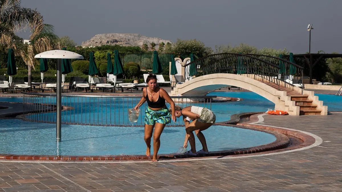 German tourists take water from a swimming pool of a hotel as they try to extinguish a fire near the seaside resort of Lindos, on the Aegean Sea island of Rhodes, southeastern Greece, on Monday, July 24, 2023. A weeklong wildfire on the Greek resort island of Rhodes tore past defenses Monday, forcing more evacuations, as three major fires raged elsewhere in the country fueled by strong winds and successive heat waves that left scrubland and forests tinder-dry. (AP Photo/Petros Giannakouris)