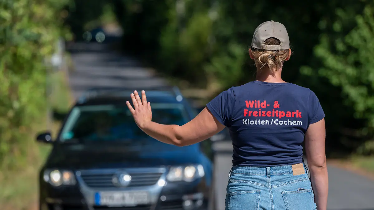 07.08.2022, Rheinland-Pfalz, Klotten: Eine Mitarbeiterin des Wild- und Freizeitparks Klotten stoppt auf der Zufahrt zum Park Besucher. Der Park ist heute geschlossen, da gestern eine Frau auf einer Achterbahn tödlich verunglückt ist und die polizeilichen Untersuchungen laufen. Foto: Harald Tittel/dpa +++ dpa-Bildfunk +++