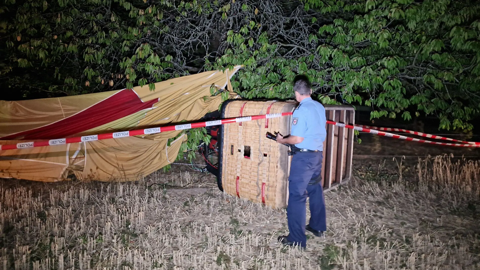 08.08.2022, Brandenburg, Beelitz: Ein Polizist inspiziert einen verunfallten Heißluftballon. Bei einem Unfall mit einem Heißluftballon ist am Montagabend ein Mann in Beelitz (Landkreis Potsdam-Mittelmark) ums Leben gekommen. Das sagte ein Polizeisprecher auf Anfrage. (zu dpa «Tödlicher Unfall mit Heißluftballon in Beelitz») Foto: Cevin Dettlaff/dpa +++ dpa-Bildfunk +++