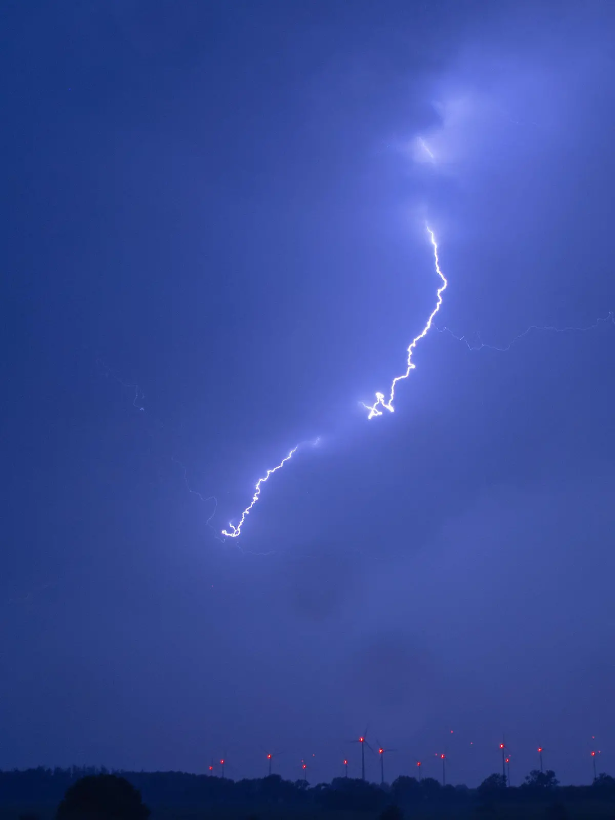 31.07.2019, Mecklenburg-Vorpommern, Pokrent: Ein Blitz ist bei einem starken Gewitter über einer Windkraftanlage zu sehen. Der Deutsche Wetterdienst hatte für Mecklenburg-Vorpommern vor örtlich starken Gewittern, teils mit Starkregen mit rund 20 Litern pro Quadratmeter in der Stunde gewarnt. Foto: Jens Büttner/dpa-Zentralbild/dpa +++ dpa-Bildfunk +++