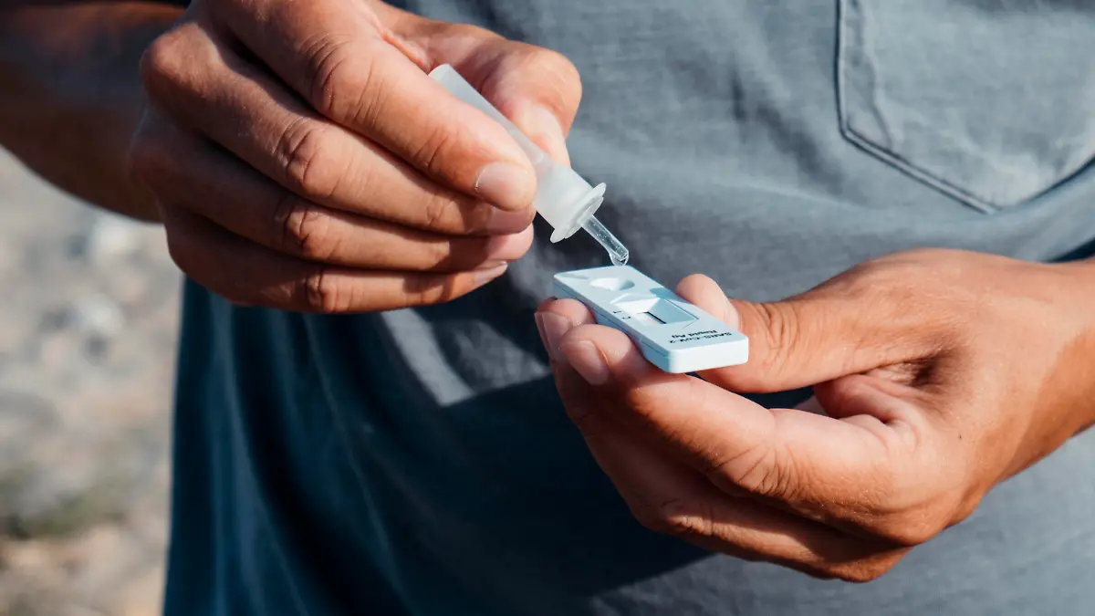 a young caucasian man outdoors, wearing a casual gray t-shirt, places the content of a pipette with his own sample into the covid-19 antigen diagnostic test device