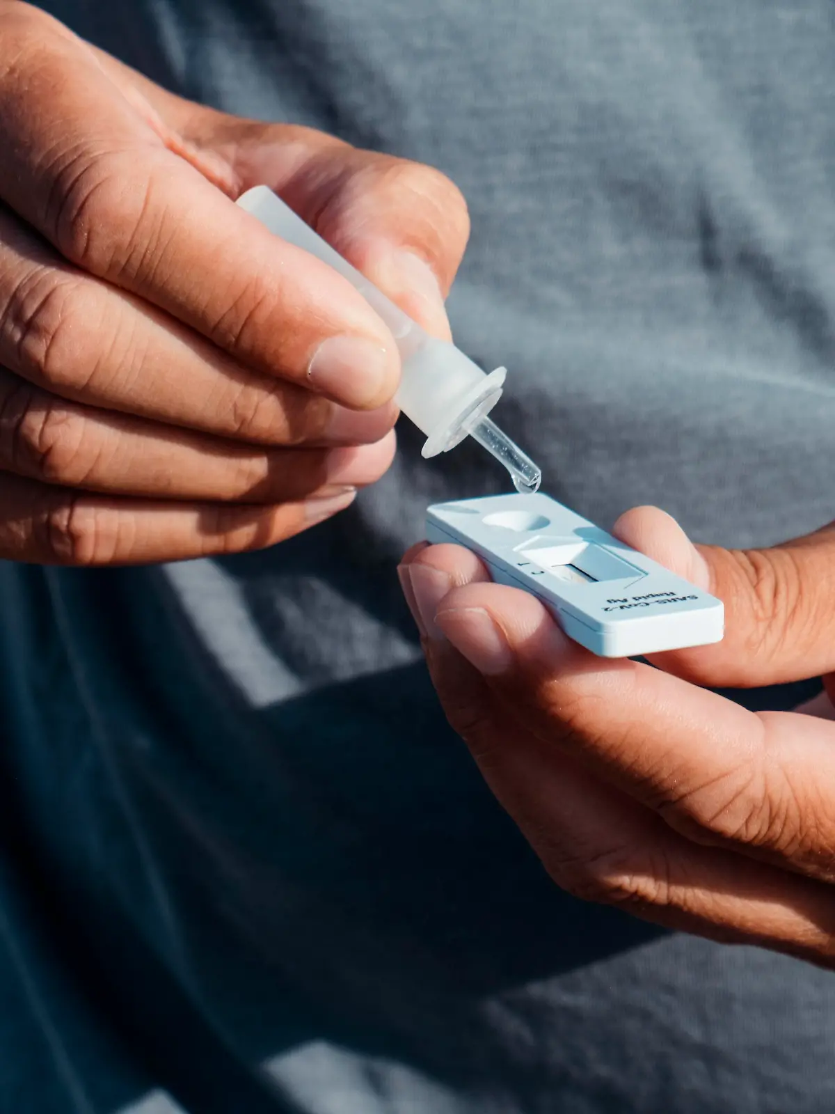 a young caucasian man outdoors, wearing a casual gray t-shirt, places the content of a pipette with his own sample into the covid-19 antigen diagnostic test device