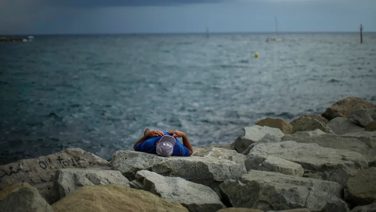 29.07.2022, Spanien, Barcelona: Ein Mann ruht sich während eines kleinen Sommersturms am Strand von Barceloneta auf einem Steg aus. Foto: Francisco Seco/AP/dpa +++ dpa-Bildfunk +++