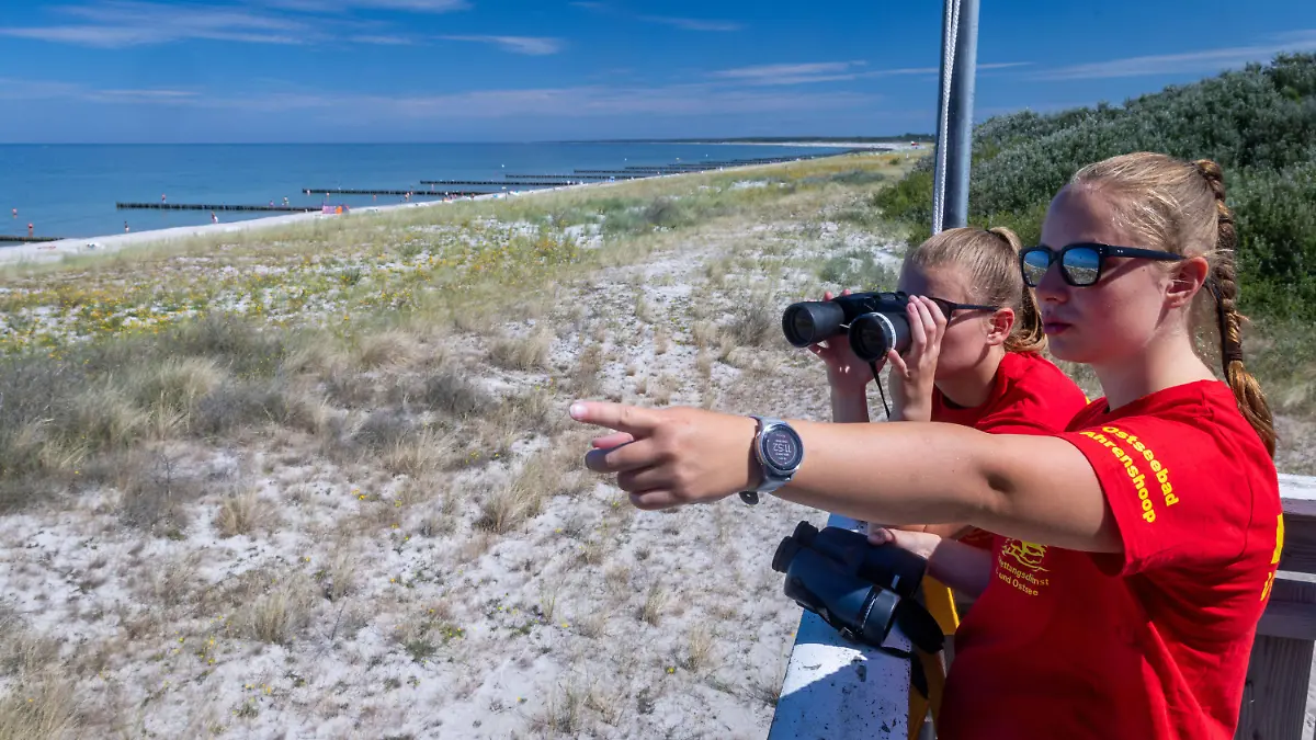 03.08.2022, Mecklenburg-Vorpommern, Ahrenshoop: Die Rettungsschwimmerinnen Linda (hinten) und Charlotte beobachten vom Hauptturm der DLRG am Ostseestrand auf der Halbinsel Darss-Fischland-Zingst den Badebetrieb. Die Deutsche Lebensrettungs-Gesellschaft (DLRG) zieht am 04.08.2022 eine erste Bilanz ihrer Arbeit zur Mitte des Sommers und veröffentlicht aktuelle bundesweite Zahlen zu Todesfällen durch Ertrinken. Foto: Jens Büttner/dpa +++ dpa-Bildfunk +++