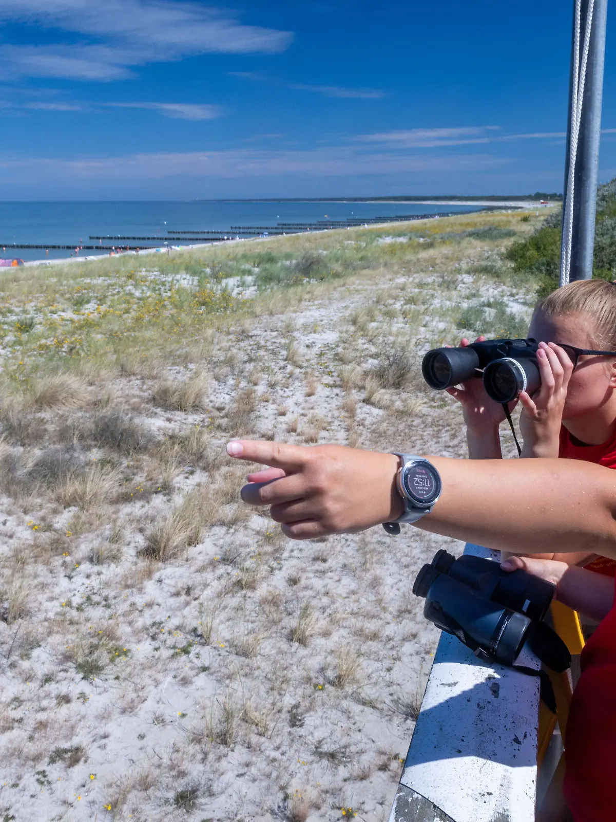 03.08.2022, Mecklenburg-Vorpommern, Ahrenshoop: Die Rettungsschwimmerinnen Linda (hinten) und Charlotte beobachten vom Hauptturm der DLRG am Ostseestrand auf der Halbinsel Darss-Fischland-Zingst den Badebetrieb. Die Deutsche Lebensrettungs-Gesellschaft (DLRG) zieht am 04.08.2022 eine erste Bilanz ihrer Arbeit zur Mitte des Sommers und veröffentlicht aktuelle bundesweite Zahlen zu Todesfällen durch Ertrinken. Foto: Jens Büttner/dpa +++ dpa-Bildfunk +++