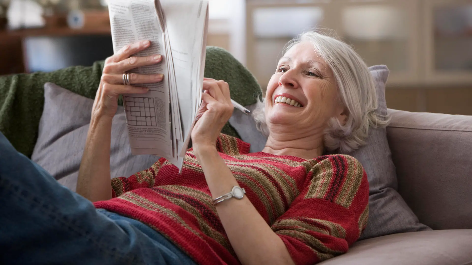 Eine Seniorin liegt auf dem Sofa und löst Kreuzworträtsel.