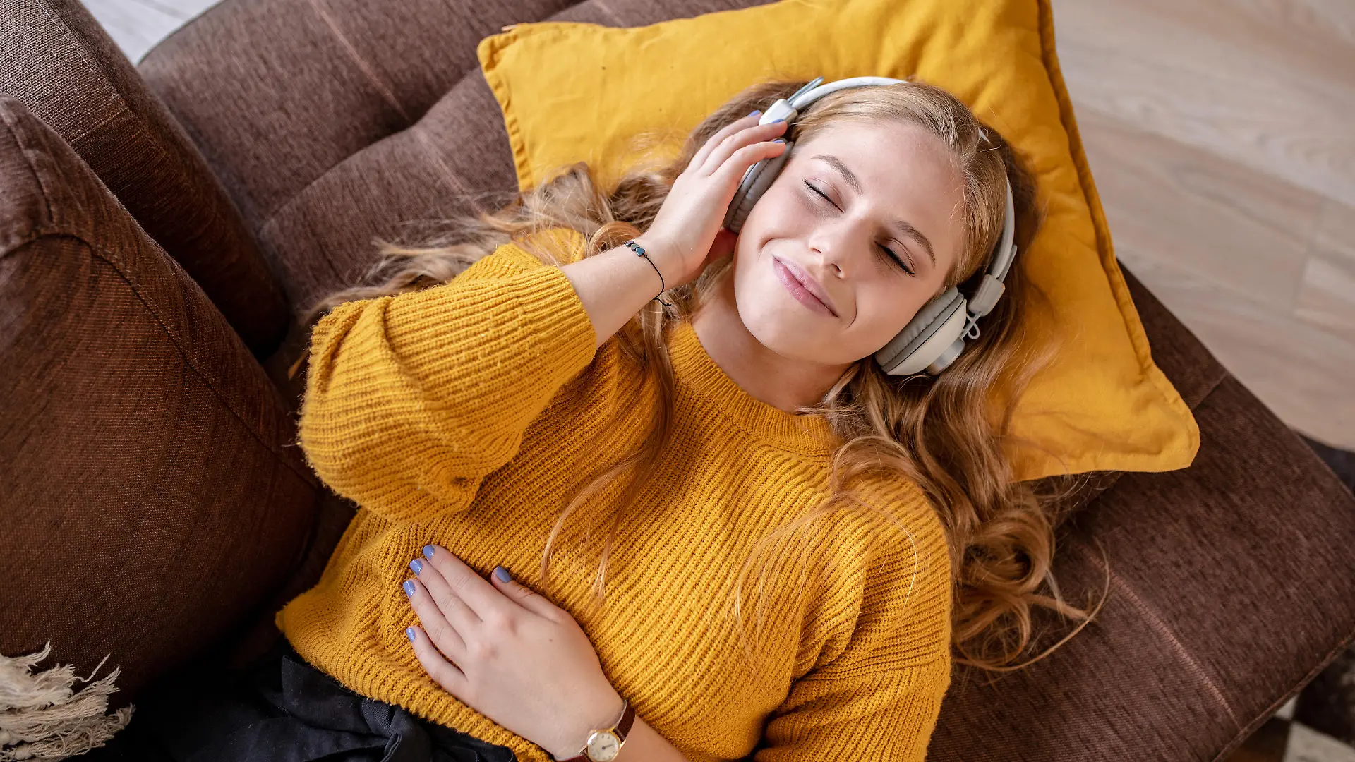 Photo of young woman with headphones laying on the couch and smiling