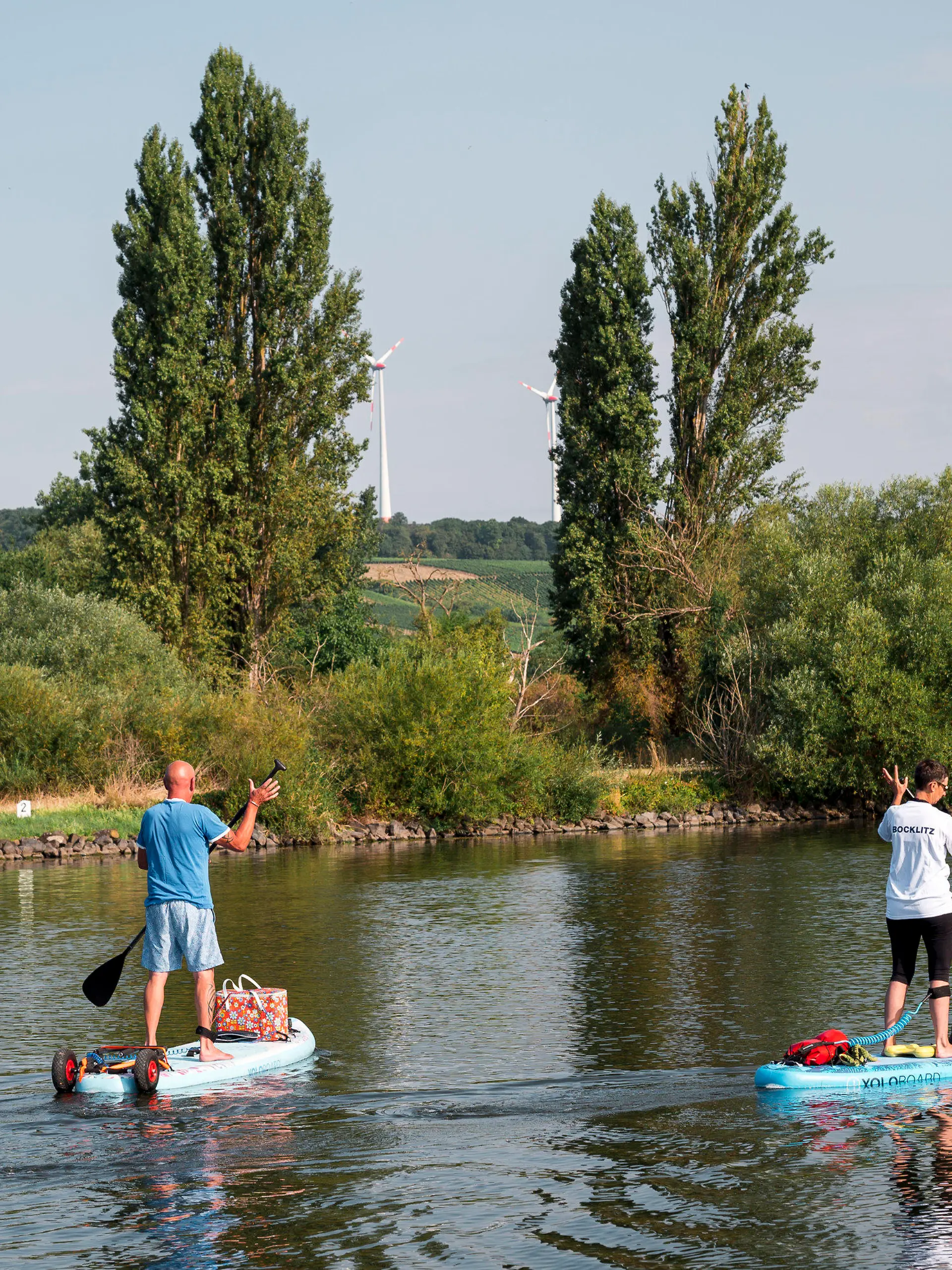 30.07.2022, Bayern, Volkach: Zwei Stand-up Paddler fahren auf dem Main zusammen mit ihrem Hund an Board entlang. Foto: Daniel Vogl/dpa +++ dpa-Bildfunk +++