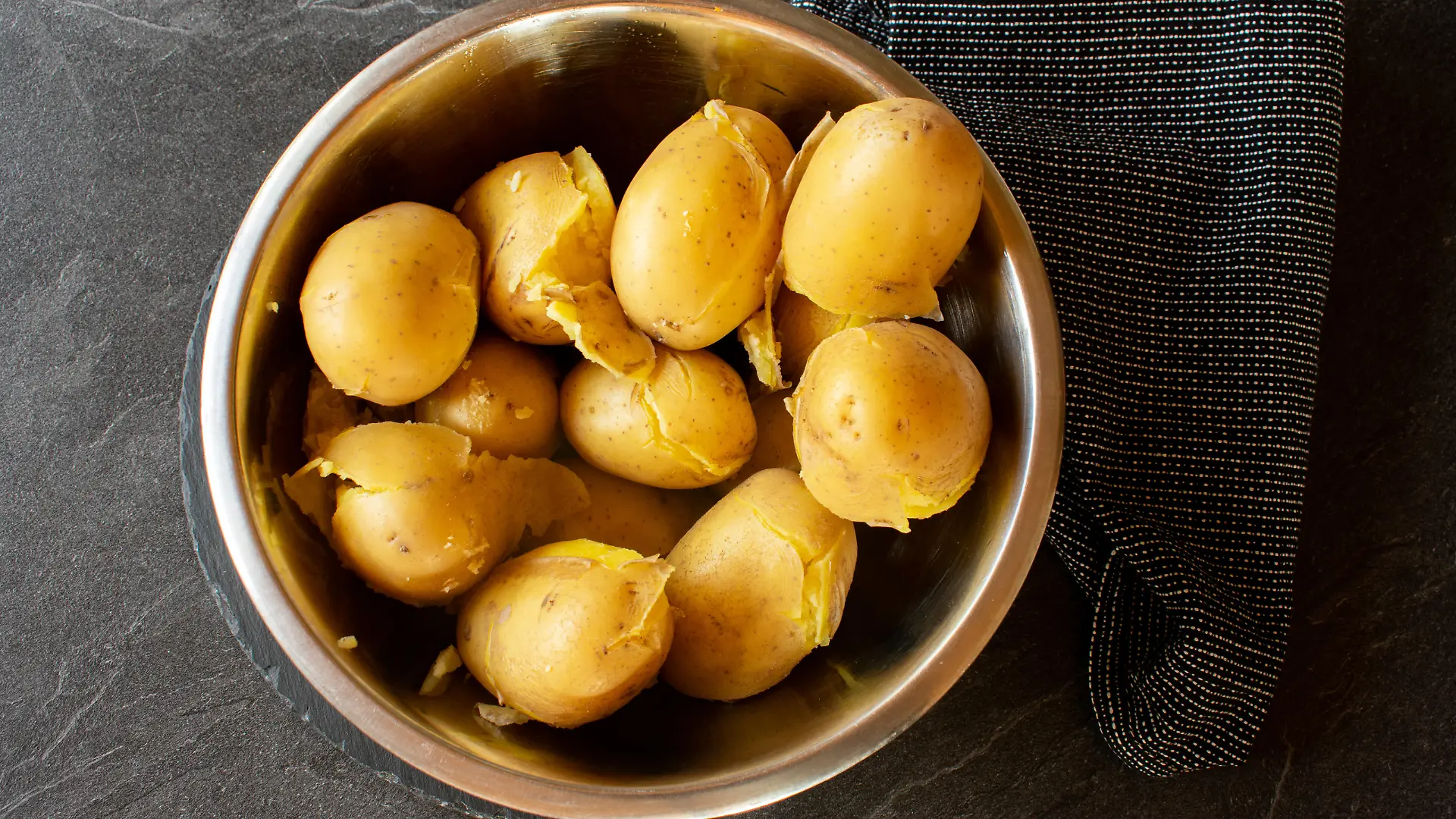 fresh cooked potatoes with skin in a bowl on dark background from above