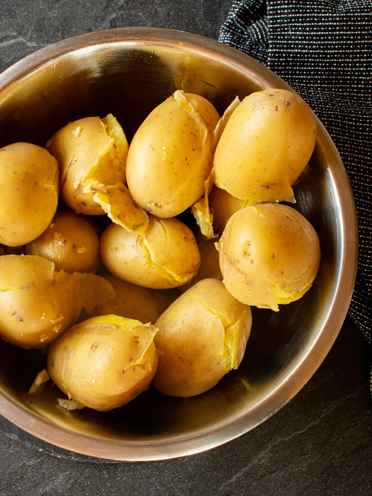 fresh cooked potatoes with skin in a bowl on dark background from above