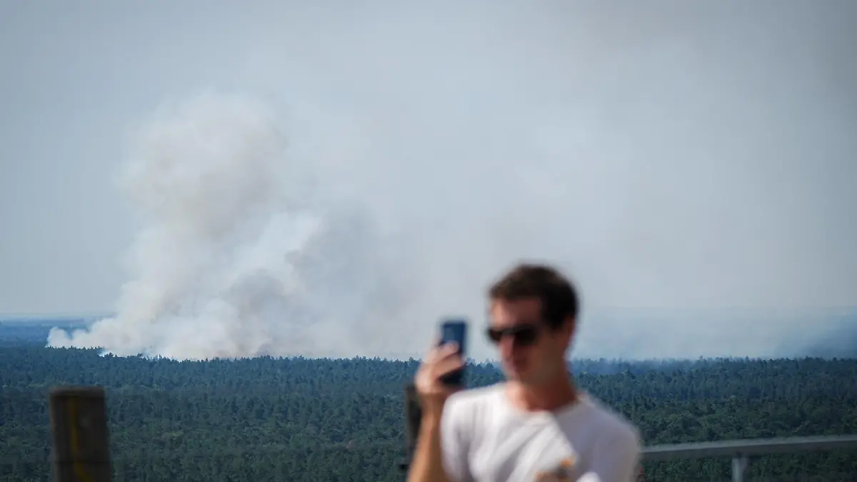dpatopbilder - 04.08.2022, Berlin: Rauch steigt hinter einem Touristen auf dem Teufelsberg bei einem Brand im Grunewald auf. Wegen eines Brandes im Grunewald wurde die Avus und der angrenzende S-Bahn-Verkehr gesperrt. Im Berliner Grunewald ist nach einer unbeabsichtigten Explosion auf dem dortigen Sprengplatz am Donnerstagmorgen ein Feuer ausgebrochen und hat den angrenzenden Wald in Brand gesetzt. Foto: Kay Nietfeld/dpa +++ dpa-Bildfunk +++