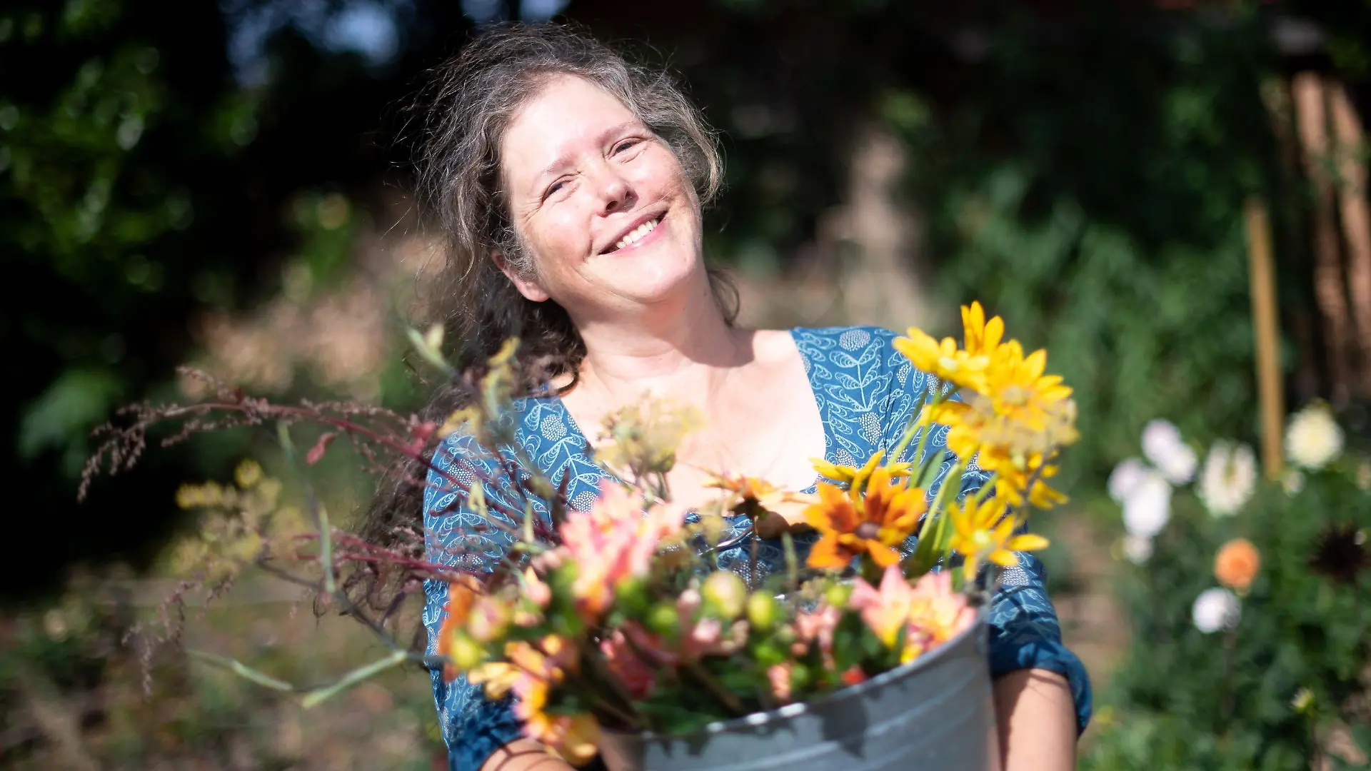 PRODUKTION - 29.07.2022, Bremen: Claudia Werner steht mit einem Eimer mit frisch geschnittenen Blumen in ihrem Garten. Die Bewegung SlowFood ist längst keine Randerscheinung mehr, nun gibt es auch die bundesweite Bewegung SlowFlowers. Mitglieder sind Floristinnen, Gärtner, Farmerinnen und Kollektive. Sie setzen sich für einen nachhaltigen, regionalen und saisonalen Schnittblumenanbau ein. (zu dpa: «Slow Flower»-Bewegung setzt auf nachhaltige Schnittblumen) Foto: Sina Schuldt/dpa +++ dpa-Bildfunk +++