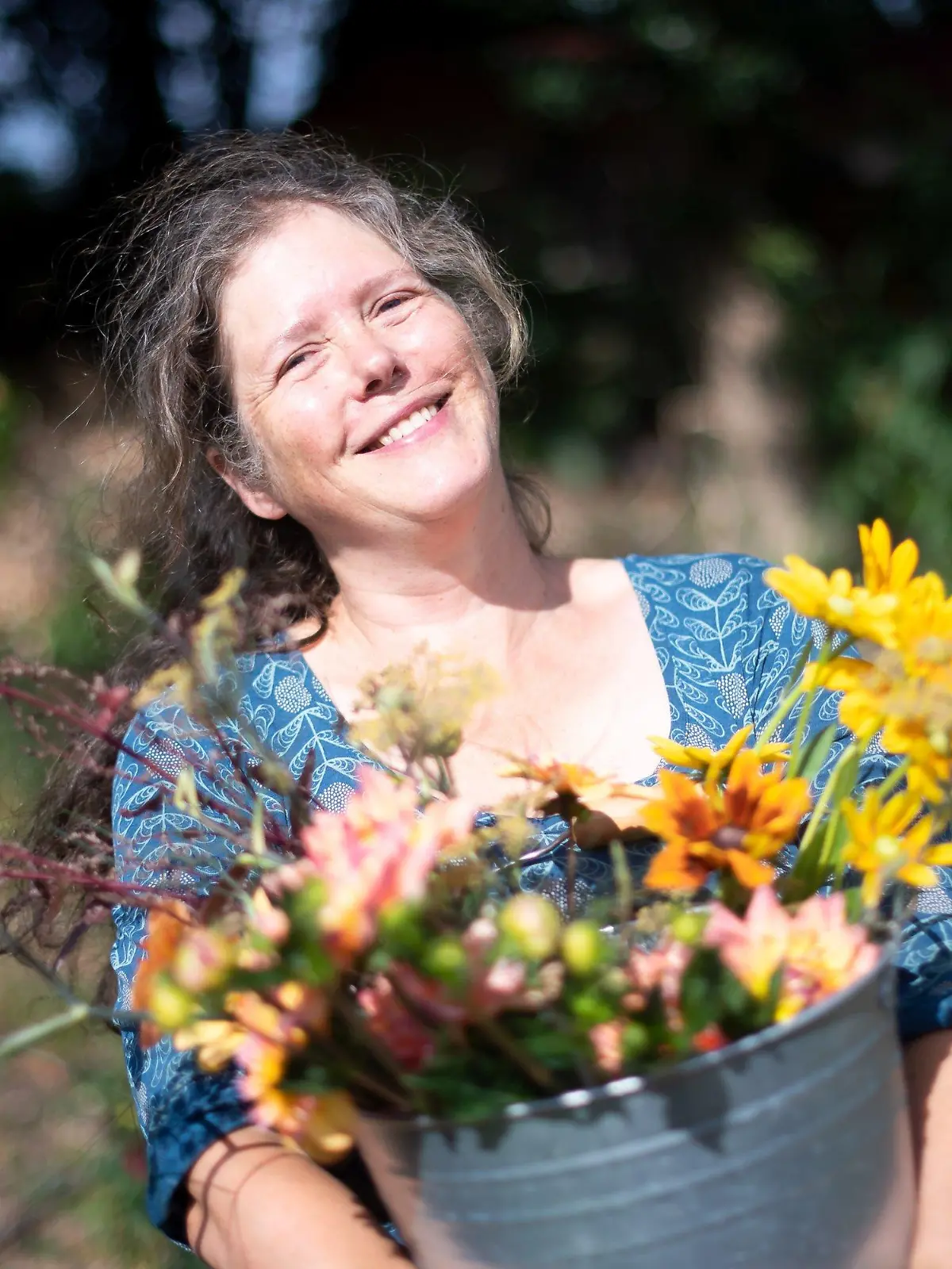 PRODUKTION - 29.07.2022, Bremen: Claudia Werner steht mit einem Eimer mit frisch geschnittenen Blumen in ihrem Garten. Die Bewegung SlowFood ist längst keine Randerscheinung mehr, nun gibt es auch die bundesweite Bewegung SlowFlowers. Mitglieder sind Floristinnen, Gärtner, Farmerinnen und Kollektive. Sie setzen sich für einen nachhaltigen, regionalen und saisonalen Schnittblumenanbau ein. (zu dpa: «Slow Flower»-Bewegung setzt auf nachhaltige Schnittblumen) Foto: Sina Schuldt/dpa +++ dpa-Bildfunk +++