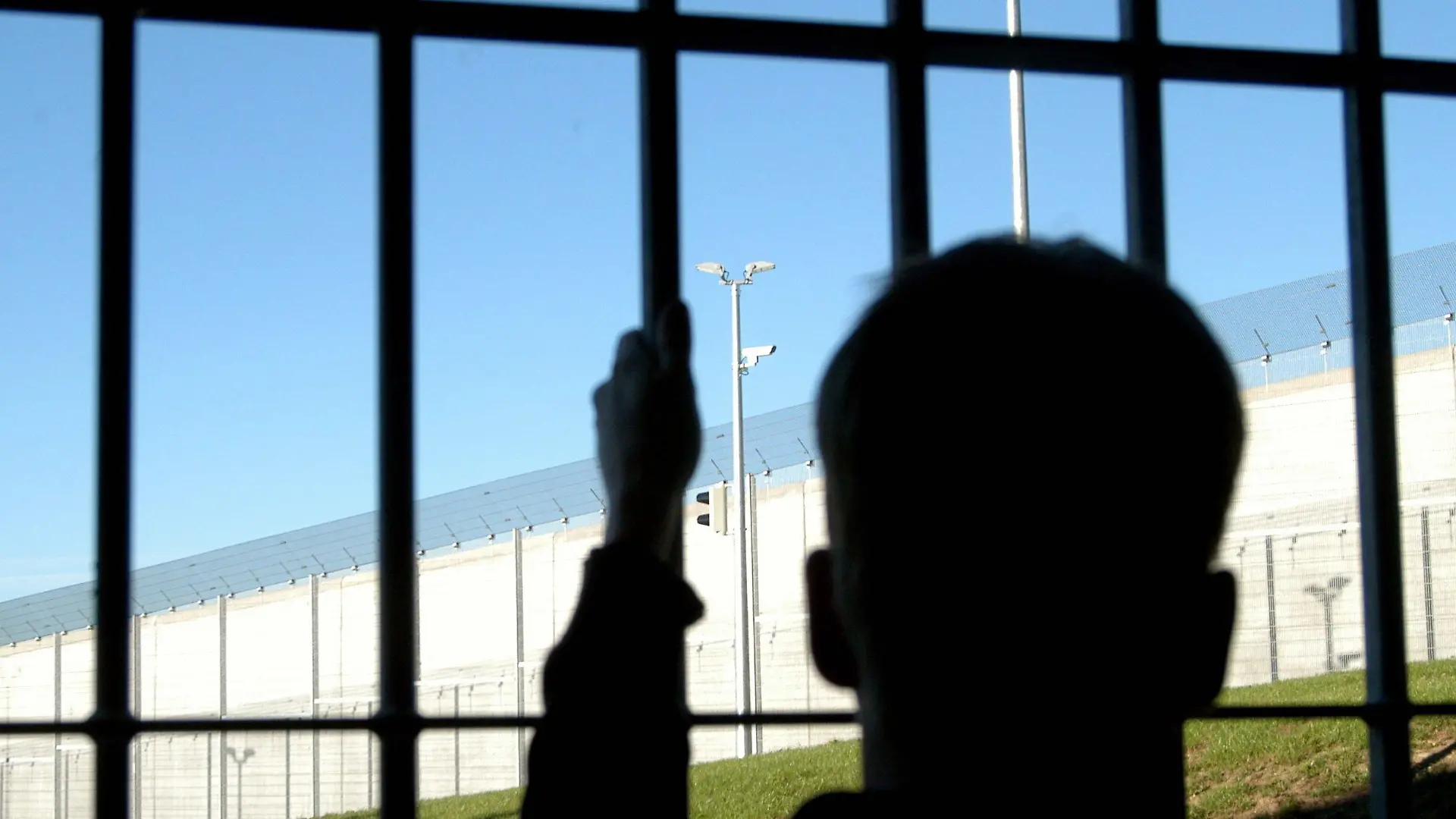 Ein Journalist steht mit einer Hand am Gitter einer Zelle der neuen Justizvollzugsanstalt im bayerischen Kempten am 4.9.2003. Er blickt auf Überwachungsanlagen mit Kameras und einer meterhohen Mauer mit Zaun. Wenige Wochen vor der Inbetriebnahme der JVA Kempten erhielten Journalisten die Möglichkeit, unter realitätsnahen Bedingungen eine Nacht hinter Gittern zu verbringen. Neben der obligatorischen Gefangenenkleidung mussten sie sich auch dem Tagesablauf in einer JVA unterordnen. Die JVA in Kempten mit 338 Haftplätzen wurde für mehr als 40 Millionen Euro errichtet und nimmt ab Oktober ihren regulären Betrieb auf.