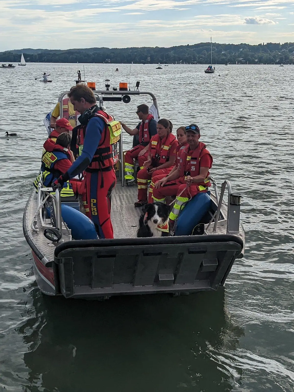 HANDOUT - 31.07.2022, Berg: Mitglieder der Wasserwacht und der DLRG sitzen während der Suche nach einem vermissten Schwimmer am Sonntag auf einem Boot im Starnberger See. Der 32-Jährige soll nach einem Zusammenstoß mit einem Motorboot untergegangen sein. (zu dpa: «Suche nach vermissten Schwimmer im Starnberger See geht weiter») Foto: Kreiswasserwacht Starnberg/dpa - ACHTUNG: Nur zur redaktionellen Verwendung im Zusammenhang mit der aktuellen Berichterstattung und nur mit vollständiger Nennung des vorstehenden Credits "Kreiswasserwacht Starnberg" +++ dpa-Bildfunk +++