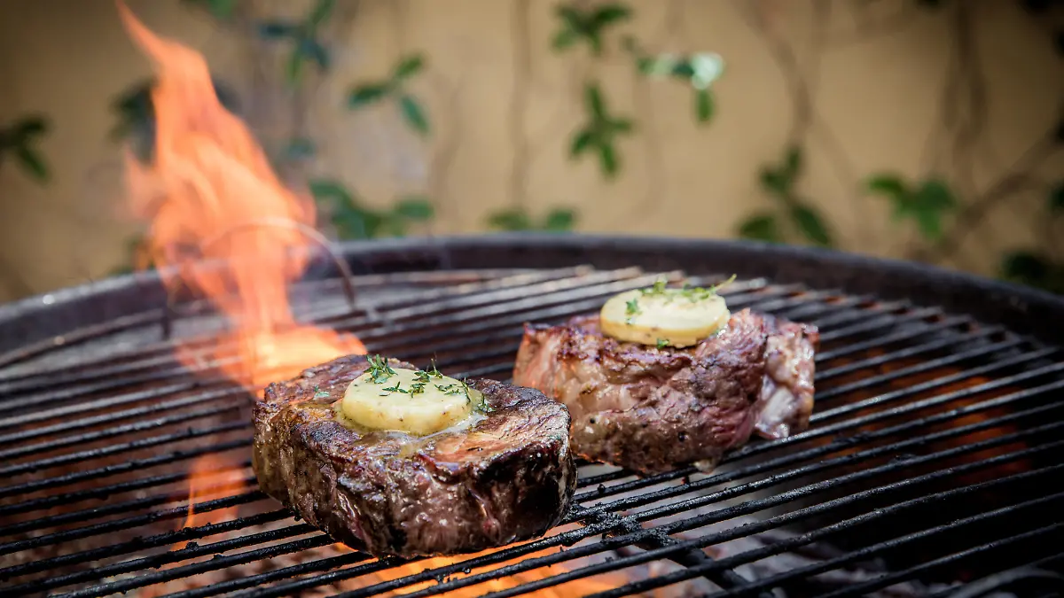 Rump steaks on the open fire. Being cooked with melted butter on the top of the meat. There is a big flame in the back ground. Busy being cooked on an open fire.