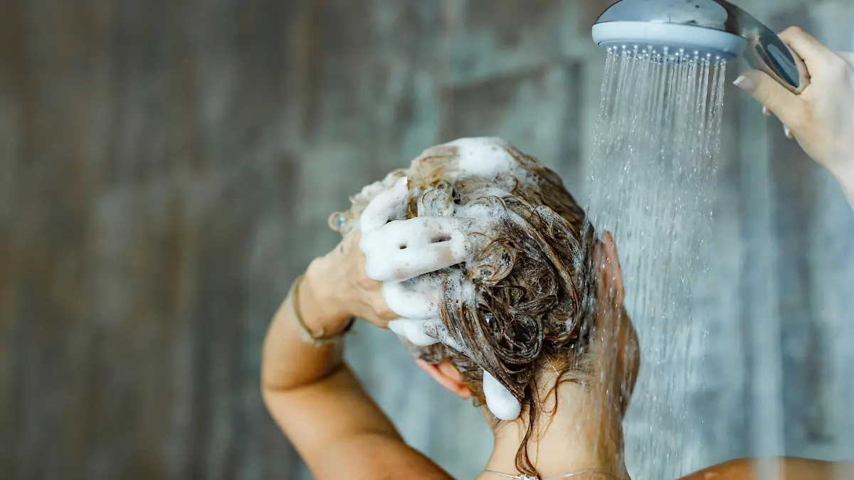 Back view of a woman washing her hair with a shampoo in bathroom. Copy space.