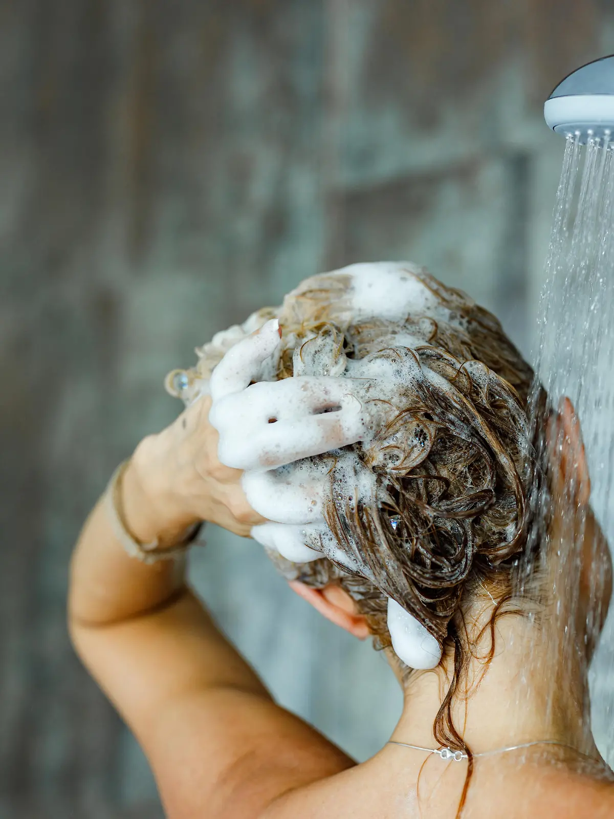 Back view of a woman washing her hair with a shampoo in bathroom. Copy space.