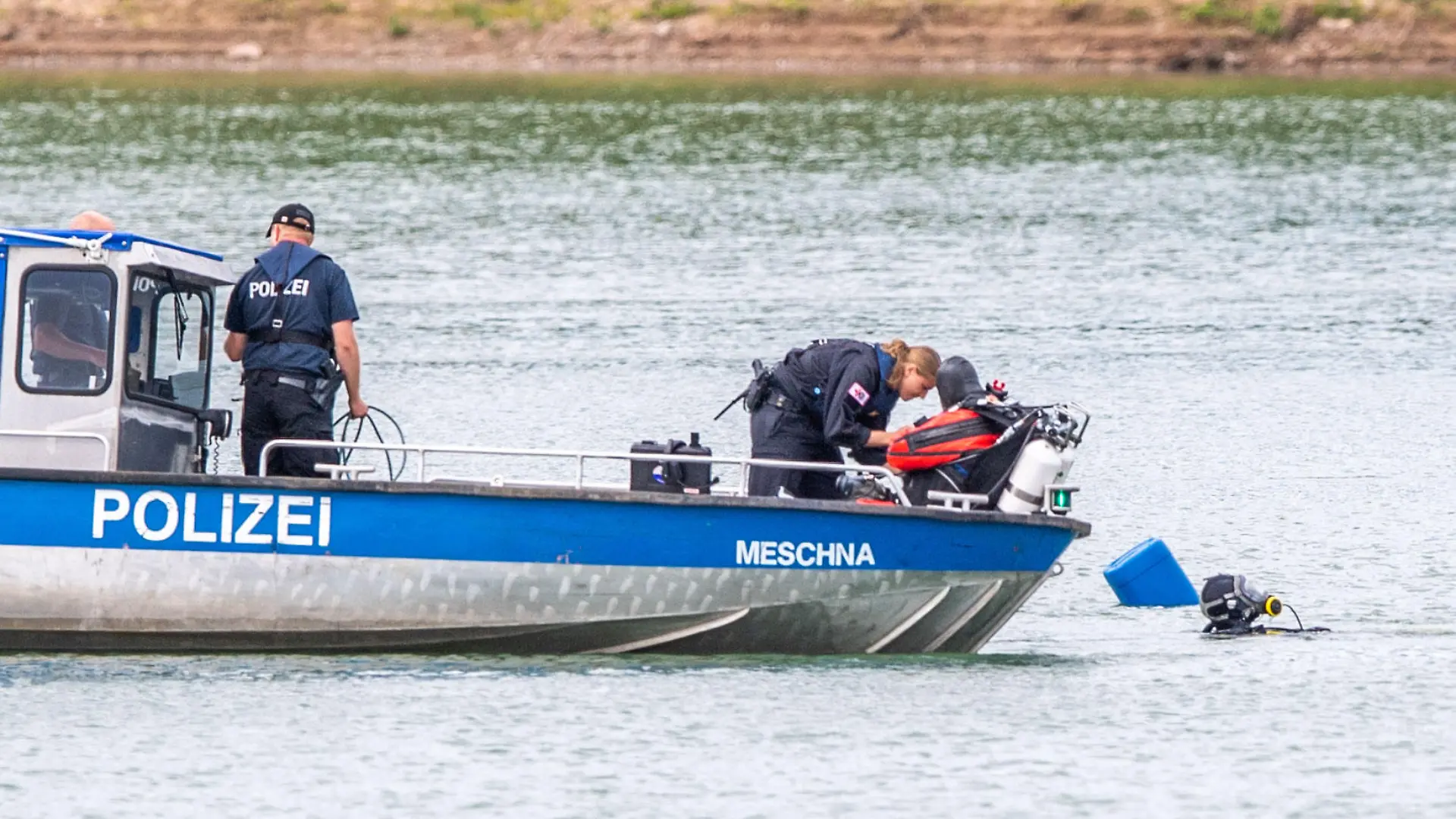 27.07.2022, Nordrhein-Westfalen, Porta Westfalica: Ein Polizeiboot mit Tauchern der Taucheinheit Bochum liegt an einer vom Sonar markierten und betonnten Stelle auf einem Kiesteich, an dem am Sonntag (24.07.2022) aus ungeklärten Gründen beim Baden zwei Personen nicht mehr aufgetaucht sind. Laut einem Sprecher der Feuerwehr sind manche Stellen des Sees rund 30 Meter tief. Fachleute der Polizei wollen nun mit einer Unterwassersonde nach den zwei Personen suchen. Foto: Lino Mirgeler/dpa +++ dpa-Bildfunk +++