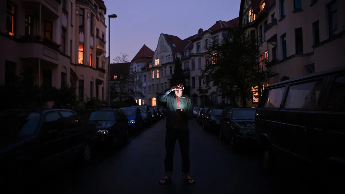 Ein Mann steht am Mittwoch (13.07.2011) während eines Stromausfalls in der Nordstadt in Hannover und schaut auf das Display seines Handys. Aus einigen Wohnungen schimmert Kerzenschein. Ein Stromausfall hat am Mittwochabend das gesamte Stadtgebiet von Hannover und anliegende Gemeinden verdunkelt. Foto: Christian Burkert dpa/lni