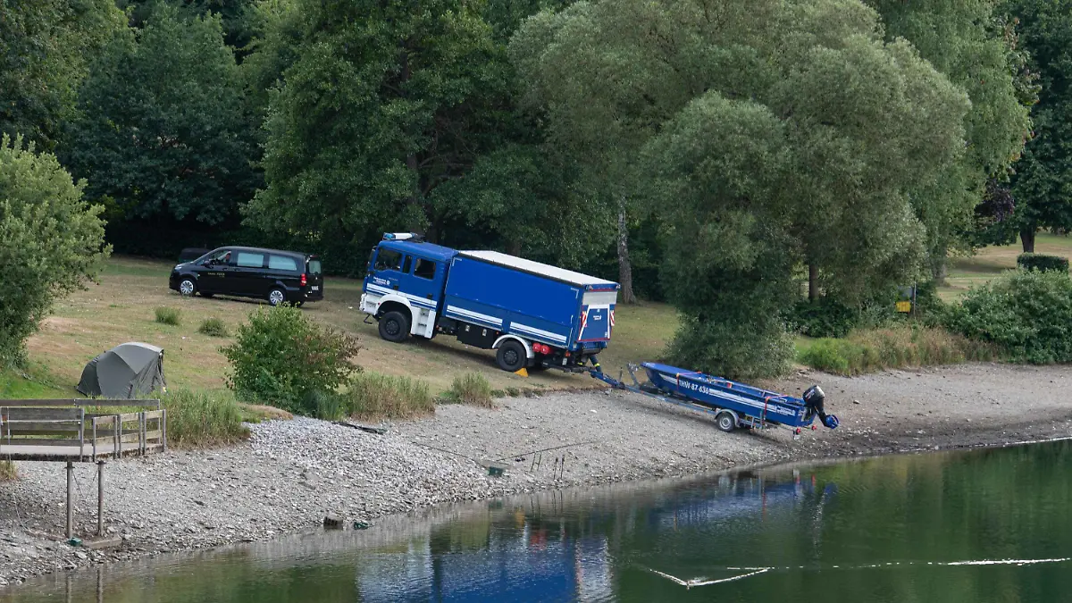 30.07.2022, Nordrhein-Westfalen, Simmerath: Ein Leichenwagen und ein Fahrzeug mit Boot des Technischen Hilfswerks (THW) stehen am Eiserbachsee. Ein 16 Jahre alter Junge ist in einem Badesee in Simmerath (Städteregion Aachen) untergegangen und gestorben. Der Jugendliche war am Samstagnachmittag in Begleitung eines Zehnjährigen in das Gewässer im Ortsteil Rurberg gesprungen, wie ein Polizeisprecher sagte. Beide waren offenbar Nichtschwimmer und drohten unterzugehen. Ersthelfern gelange es nach Angaben des Sprechers, das jüngere Kind zu retten. Der 16-Jährige wurde zwei Stunden später von Tauchern leblos aus dem Wasser geborgen. Foto: Vincent Kempf/dpa +++ dpa-Bildfunk +++