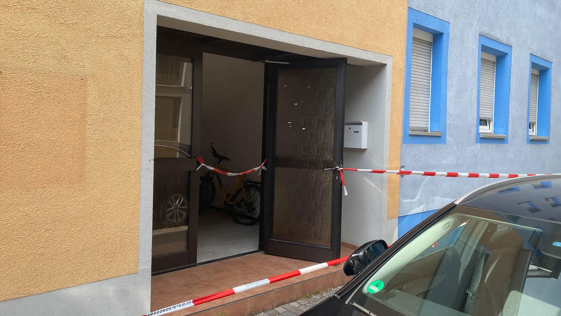 30.07.2022, Baden-Württemberg, Offenburg: Ein Blick auf einen mit Polizei-Absperrband abgeriegelten Hauseingang. In einem Zimmer in einer Unterkunft in Offenburg sind am Samstag zwei tote Frauen entdeckt worden. Foto: Marco Dürr/Einsatz-Report24/dpa - ACHTUNG: Nummer auf Auto wurde aus rechtlichen Gründen gepixelt +++ dpa-Bildfunk +++