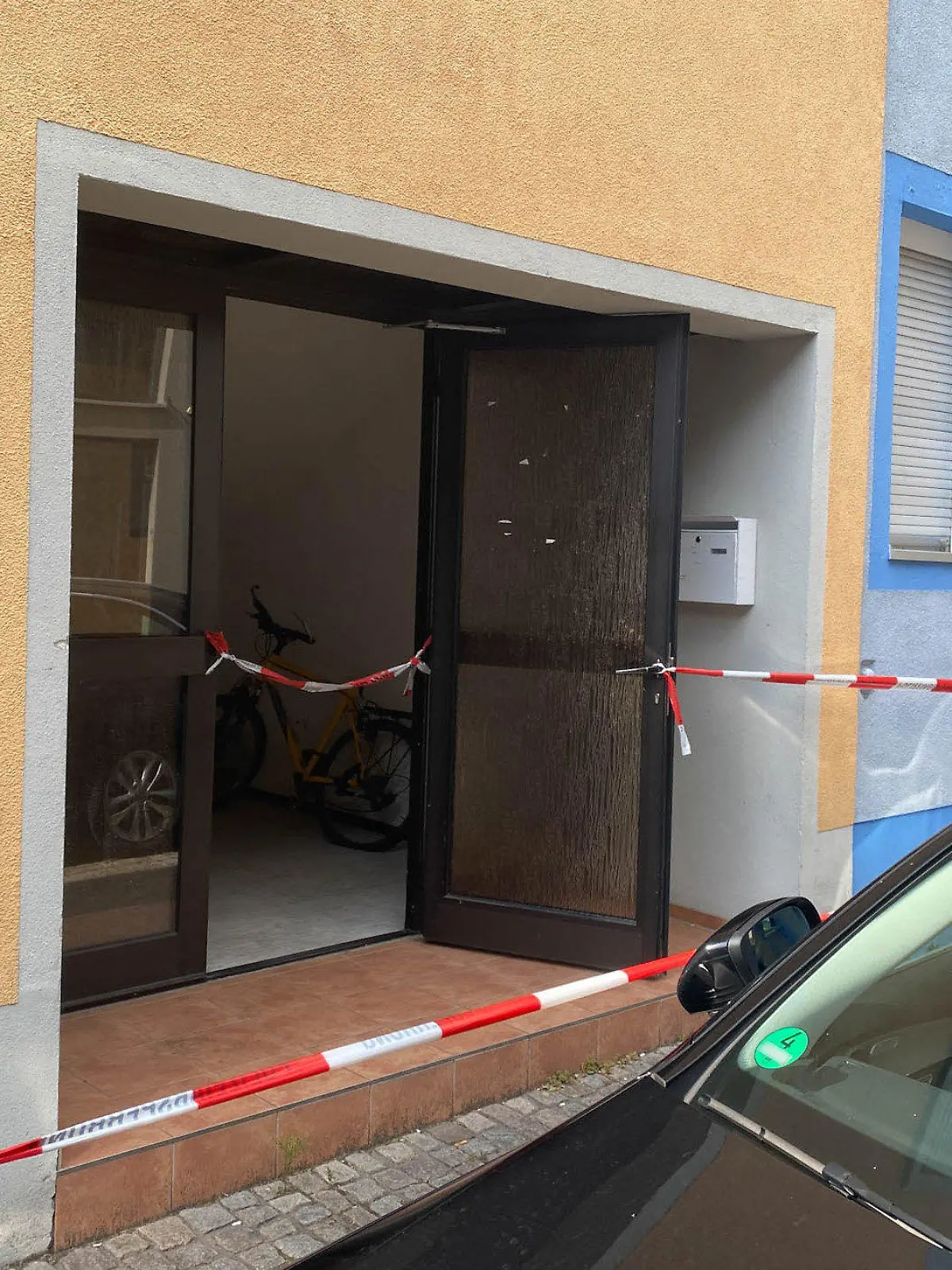 30.07.2022, Baden-Württemberg, Offenburg: Ein Blick auf einen mit Polizei-Absperrband  abgeriegelten Hauseingang. In einem Zimmer in einer Unterkunft in Offenburg sind am Samstag zwei tote Frauen entdeckt worden. Foto: Marco Dürr/Einsatz-Report24/dpa - ACHTUNG: Nummer auf Auto wurde aus rechtlichen Gründen gepixelt +++ dpa-Bildfunk +++